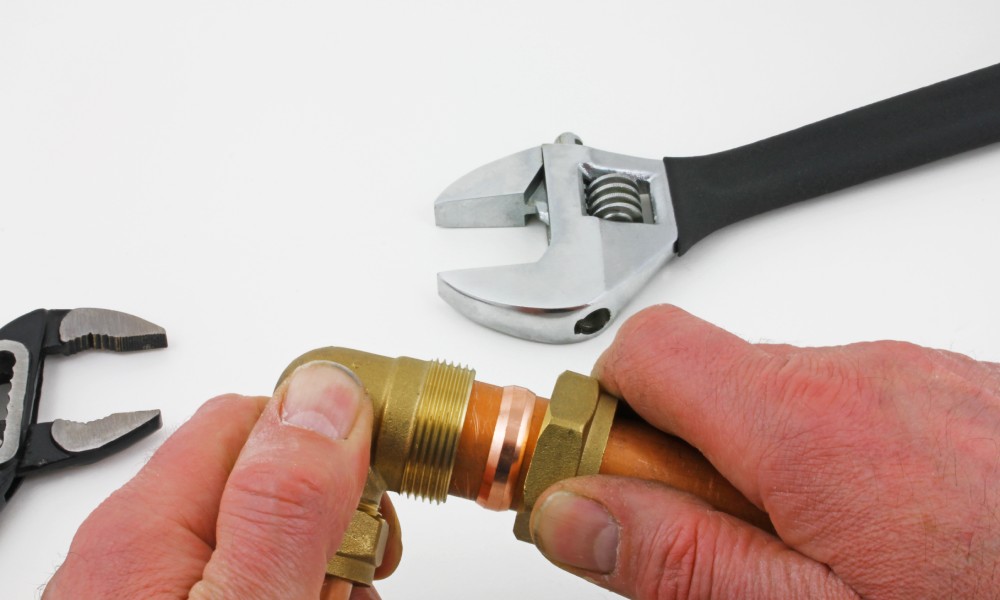 A man holds a brass compression fitting body and compression nut on copper piping with a copper ferule around it.