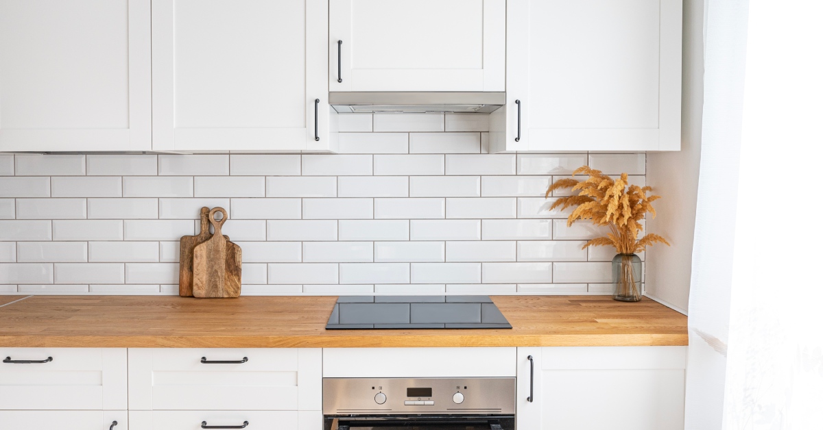 A minimalist kitchen with white countertops and drawers with a small electric stovetop, oven, and wood countertop.