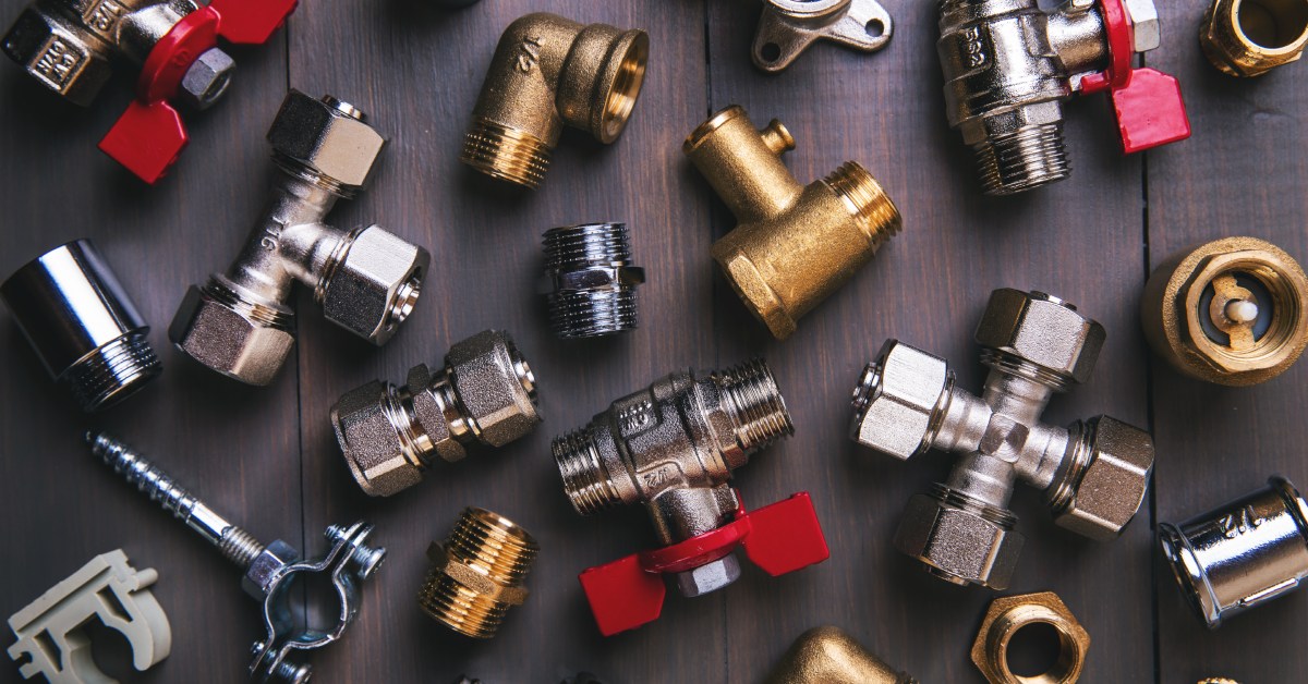 A spread of various plumbing elbows, clamps, tees, and valves sit on a dark hardwood background.